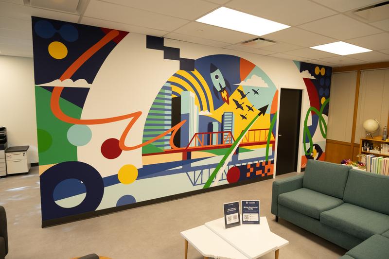 Wide view of the Signal wall at Co.Labs Saskatoon: a rocket, city skyline and the Broadway Bridge rendered in bold geometric colour.