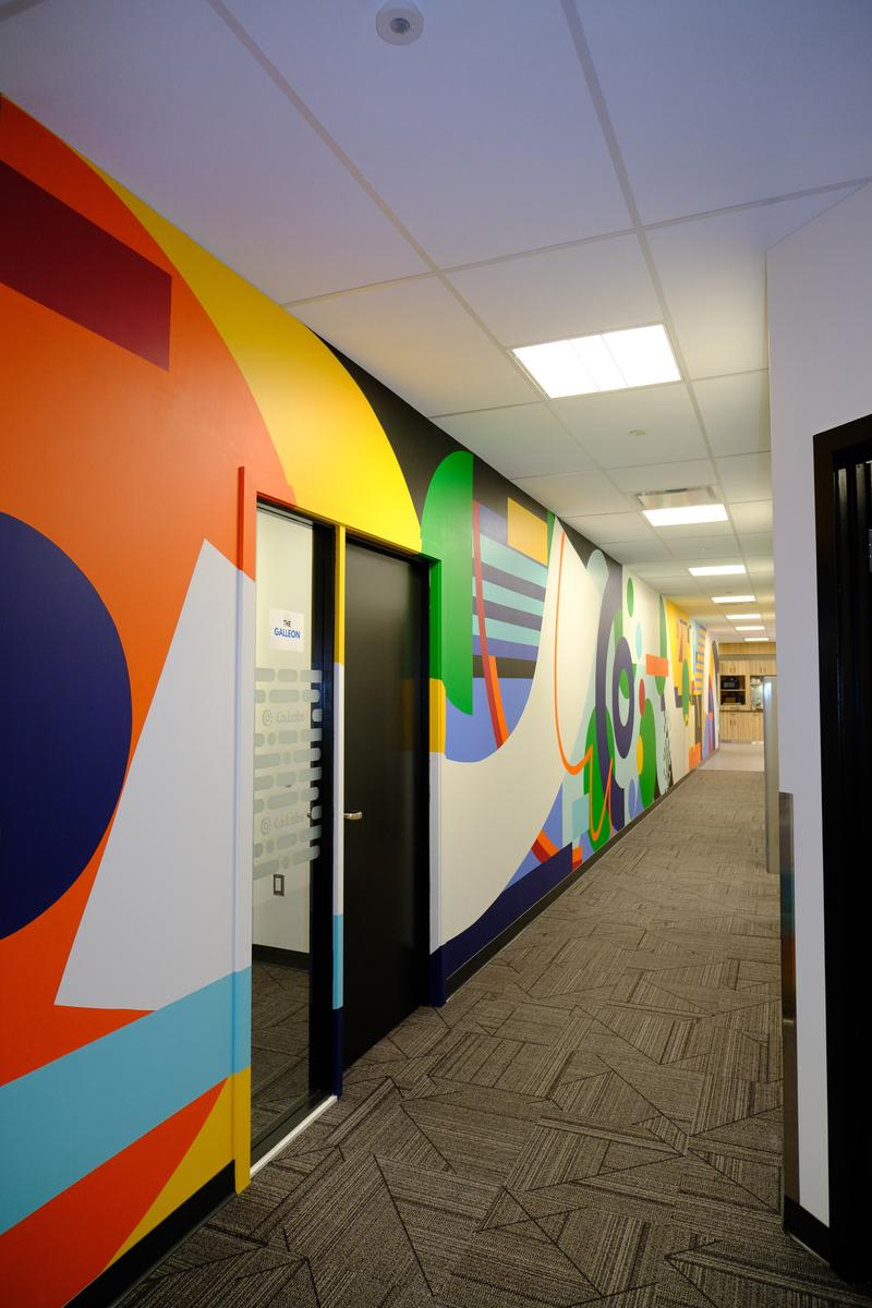 Corridor of the Co.Labs office with orange and navy geometry wrapping the entry doors and the mural continuing down the hall.