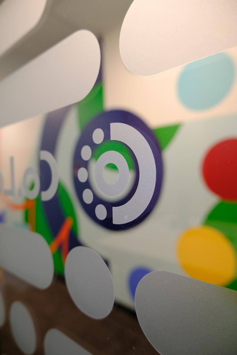 Close view of the Co.Labs logo on frosted glass, with the mural's colour forms visible behind it.