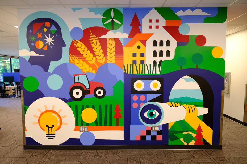 The Foundation wall seen straight on: a profile head filled with geometric shapes, wheat, a tractor, houses, a lightbulb and a telescope.