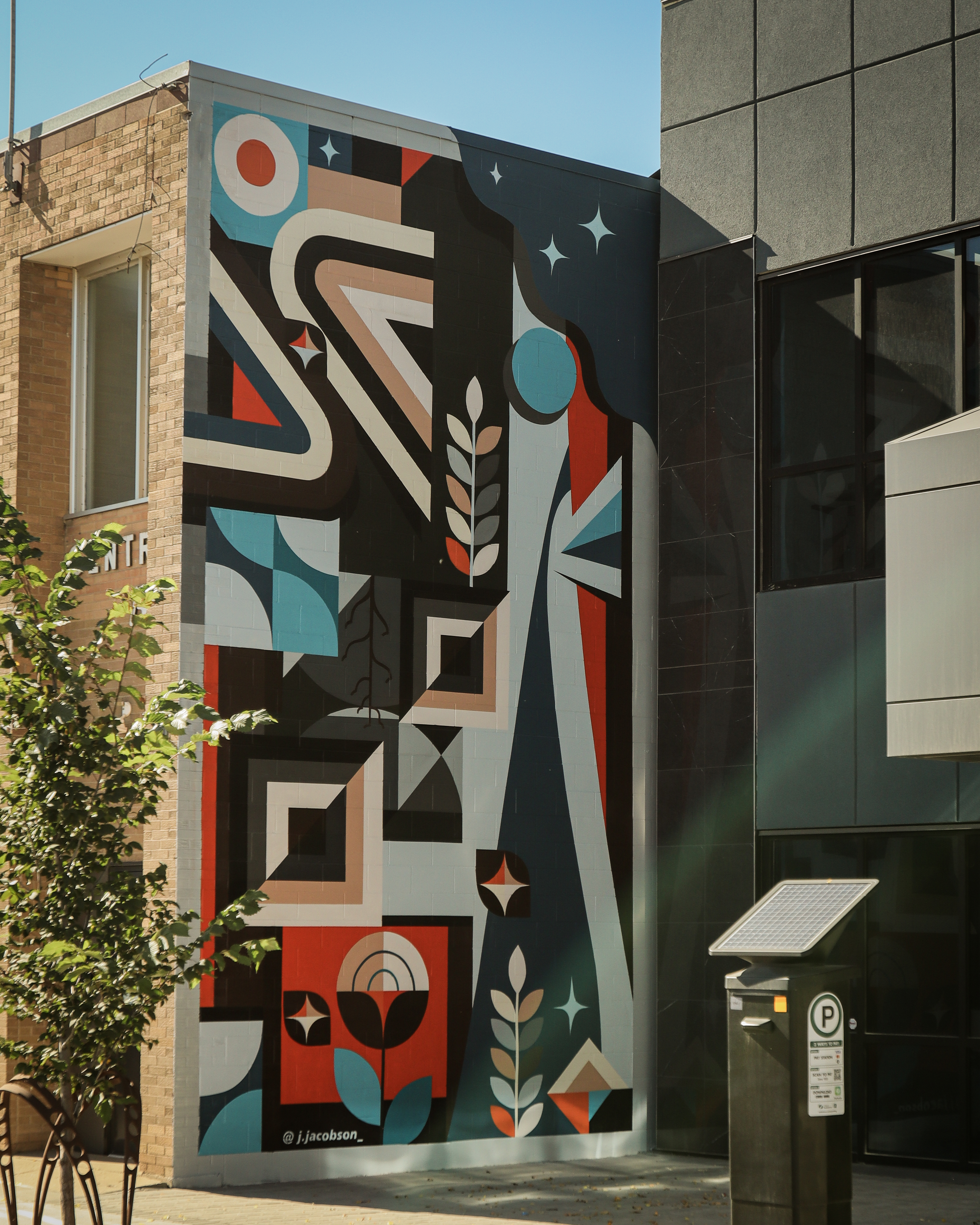 Large mural on Western Ag building featuring abstract figures, geometric shapes, and floral motifs in balanced color tones.